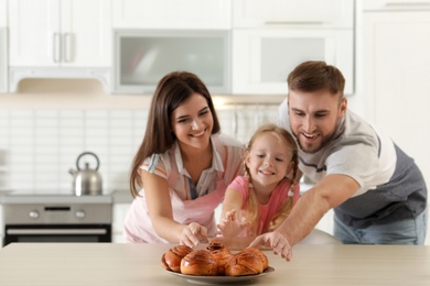 Photo of Happy family with freshly oven baked buns at table in kitchen