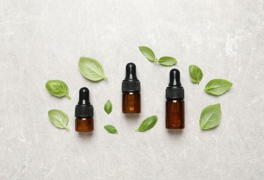 Photo of Bottles of essential basil oil and fresh leaves on light grey table, flat lay