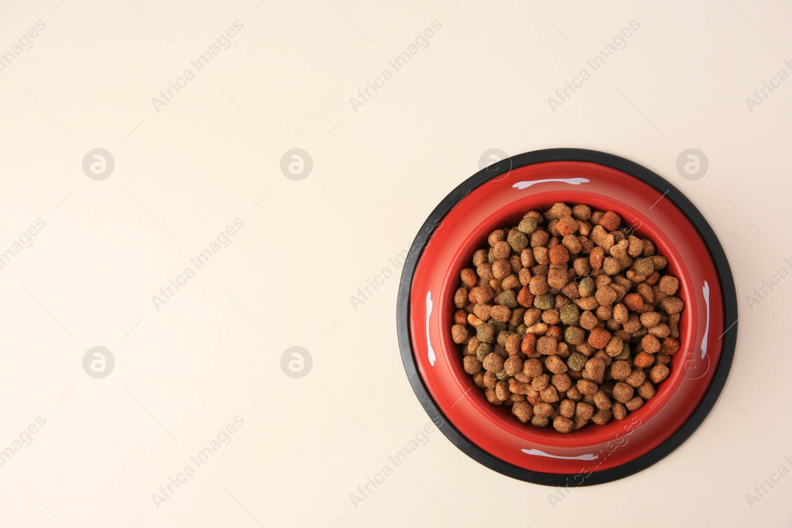 Photo of Dry dog food in feeding bowl on beige background, top view. Space for text