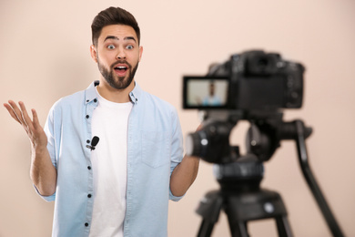 Photo of Young blogger recording video on camera against beige background