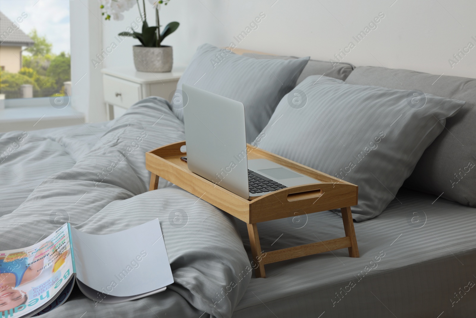 Photo of Wooden tray table with laptop on bed indoors