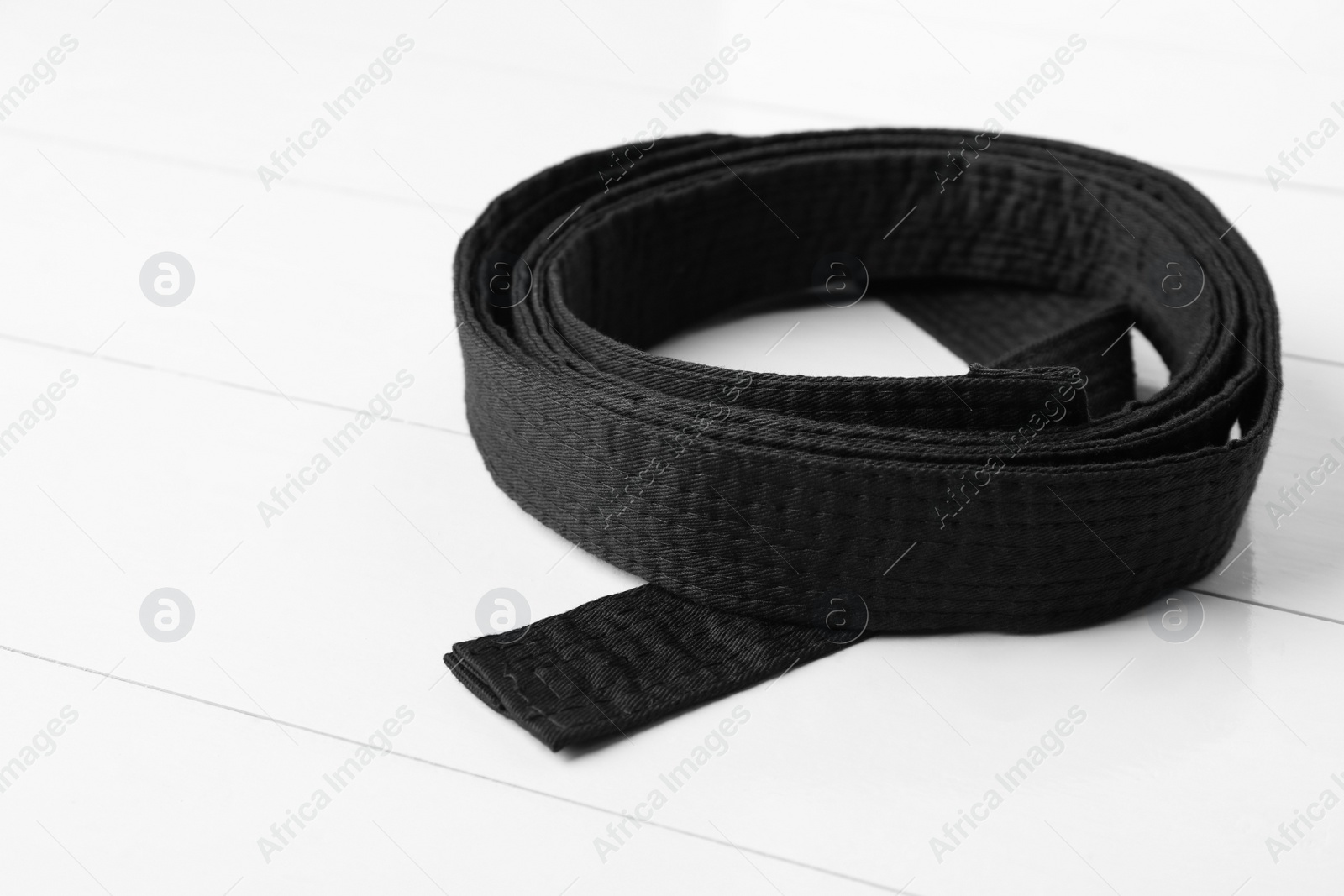 Photo of Rolled black belt on white wooden background, closeup. Oriental martial arts