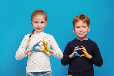 Photo of Little girl and boy making heart with their hands painted in Ukrainian flag colors on light blue background. Love Ukraine concept