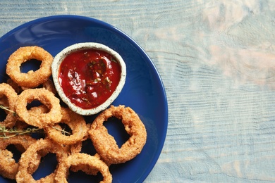 Photo of Plate with homemade crunchy fried onion rings and tomato sauce on wooden background, top view. Space for text