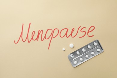 Word Menopause and pills on beige background, flat lay