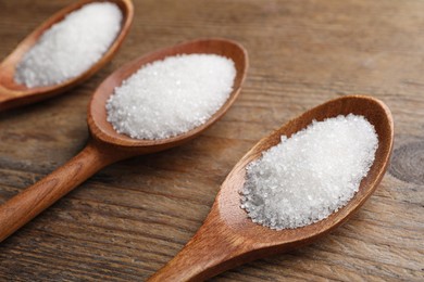 Photo of Granulated sugar in spoons on wooden table, closeup