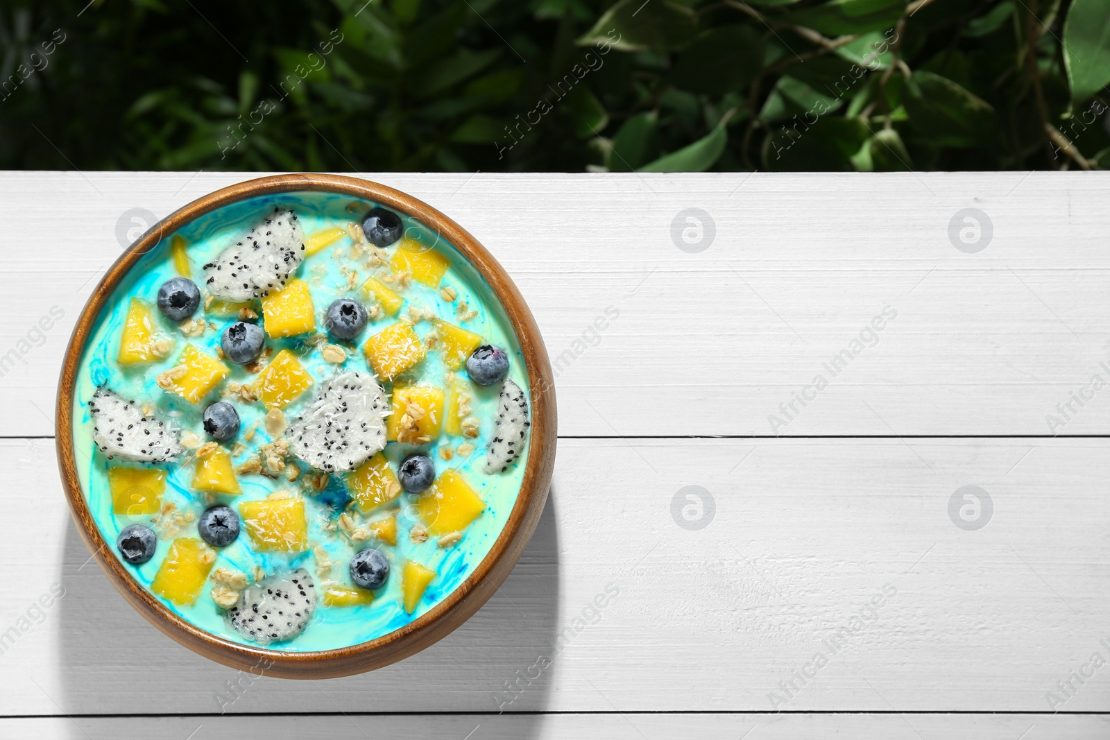 Photo of Delicious smoothie bowl with fresh fruits, blueberries and oatmeal on white wooden table outdoors, top view. Space for text