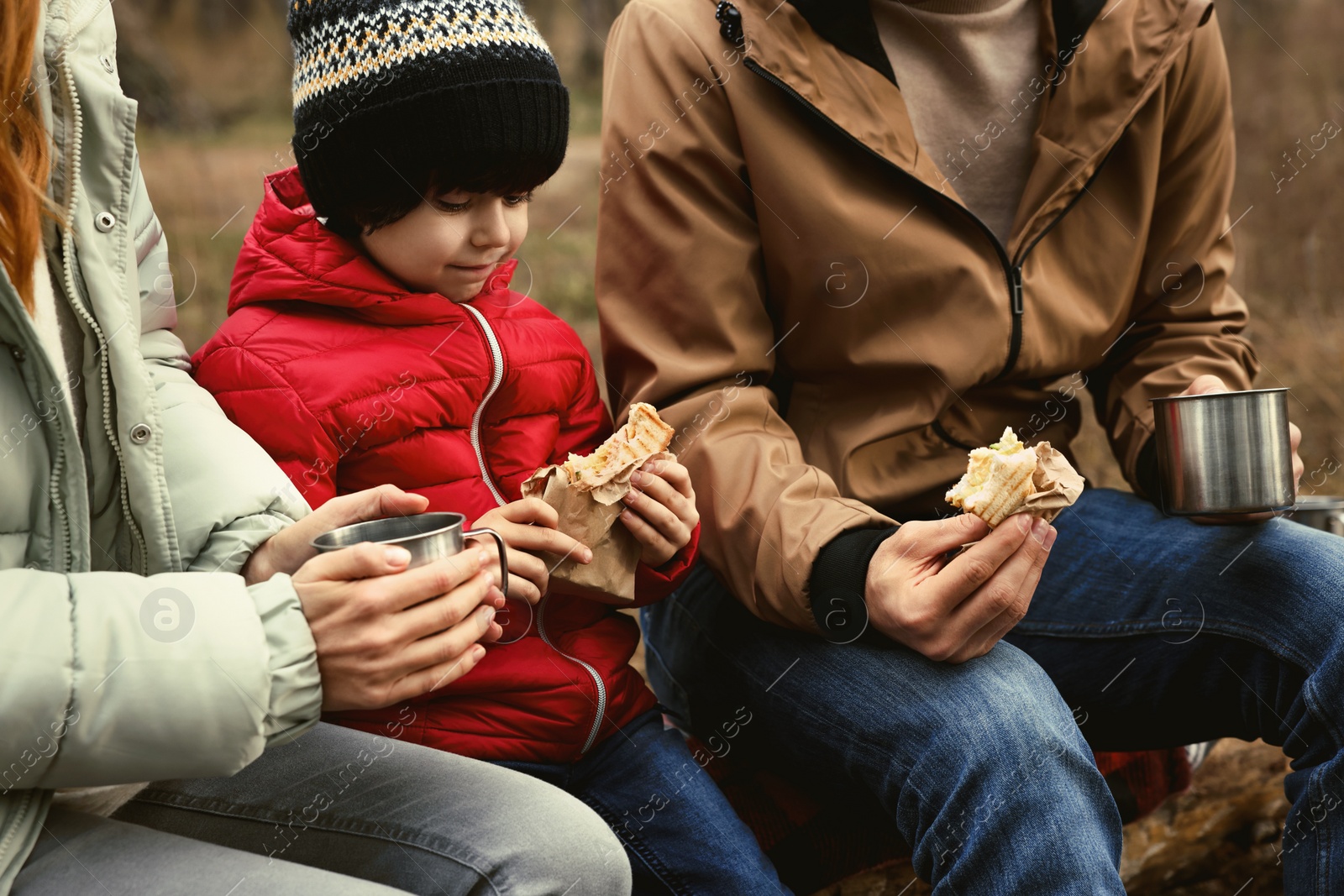 Photo of Happy family with sandwiches and hot drinks spending time together in forest, closeup