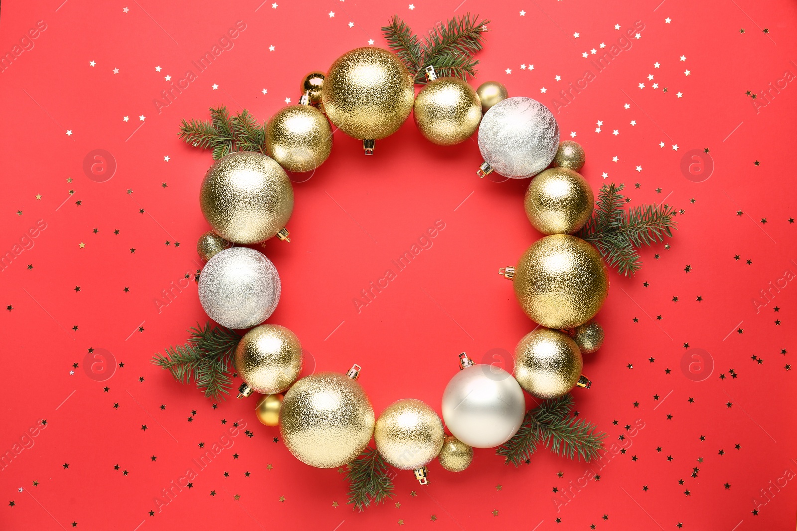Photo of Beautiful festive wreath made of color Christmas balls and fir tree branches on red background, top view