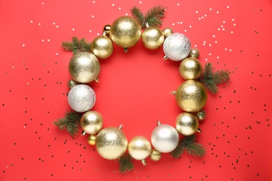 Photo of Beautiful festive wreath made of color Christmas balls and fir tree branches on red background, top view