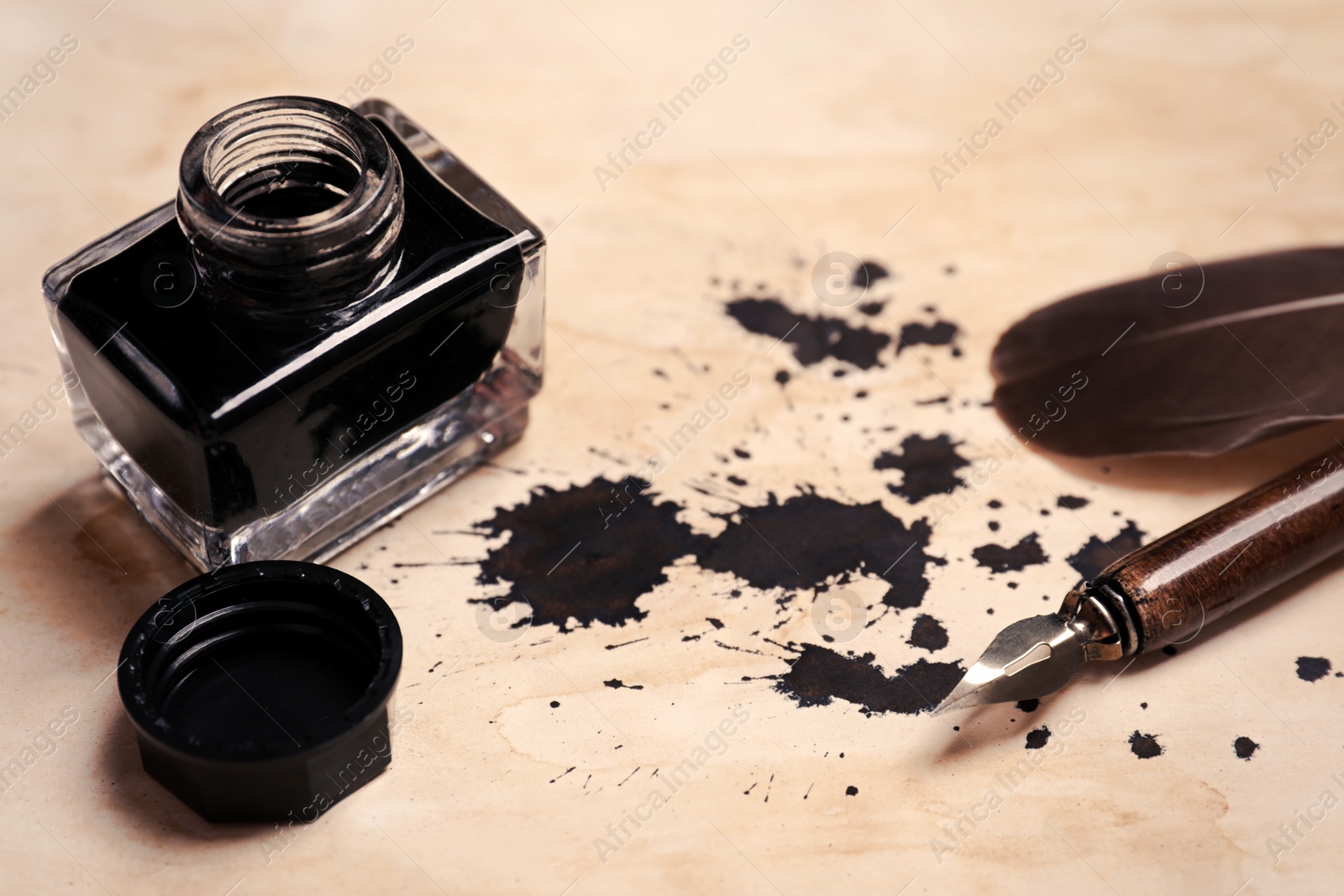 Photo of Feather, fountain pen and inkwell on vintage parchment with ink stains, closeup