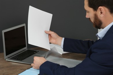Photo of Businessman putting document into punched pocket at wooden table in office, closeup