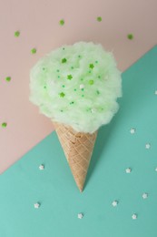 Sweet cotton candy in waffle cone on color background, top view