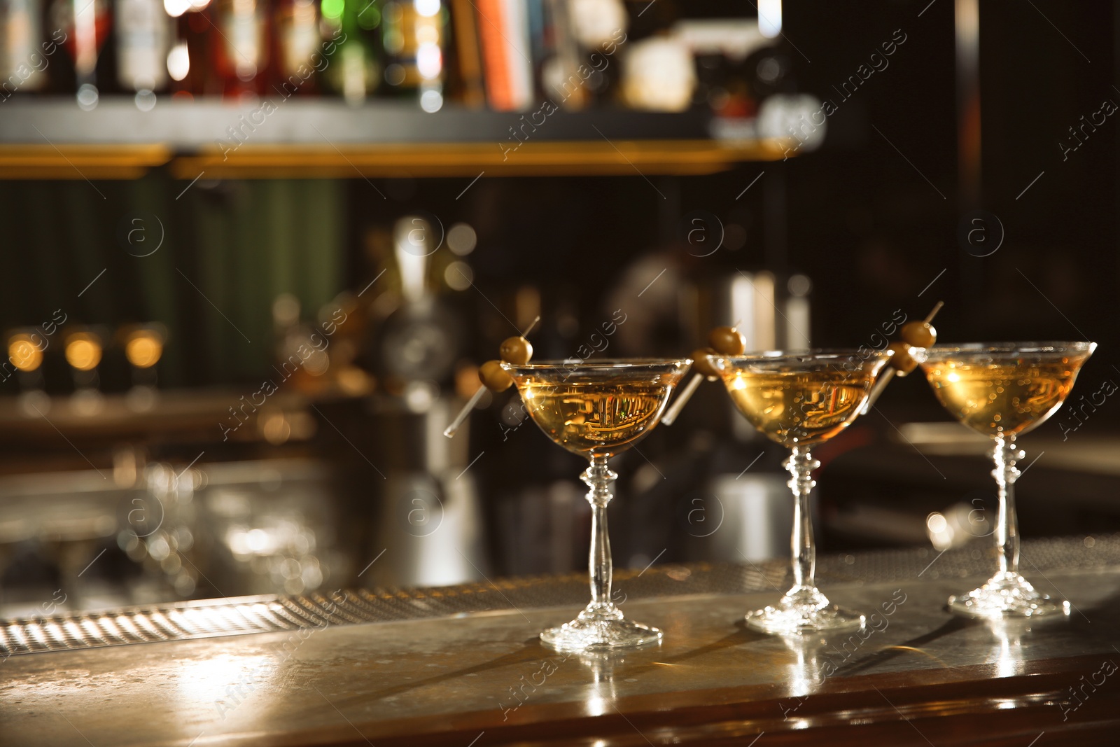 Photo of Glasses of martini cocktail with olives on bar counter. Space for text