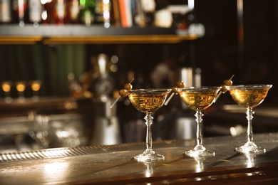 Glasses of martini cocktail with olives on bar counter. Space for text