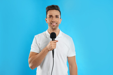 Young male journalist with microphone on blue background