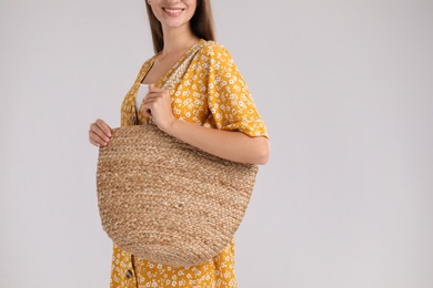 Photo of Young woman with stylish straw bag on light grey background, closeup. Space for text