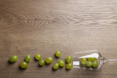 Photo of Wineglass with scattered grapes on wooden table, flat lay. Space for text