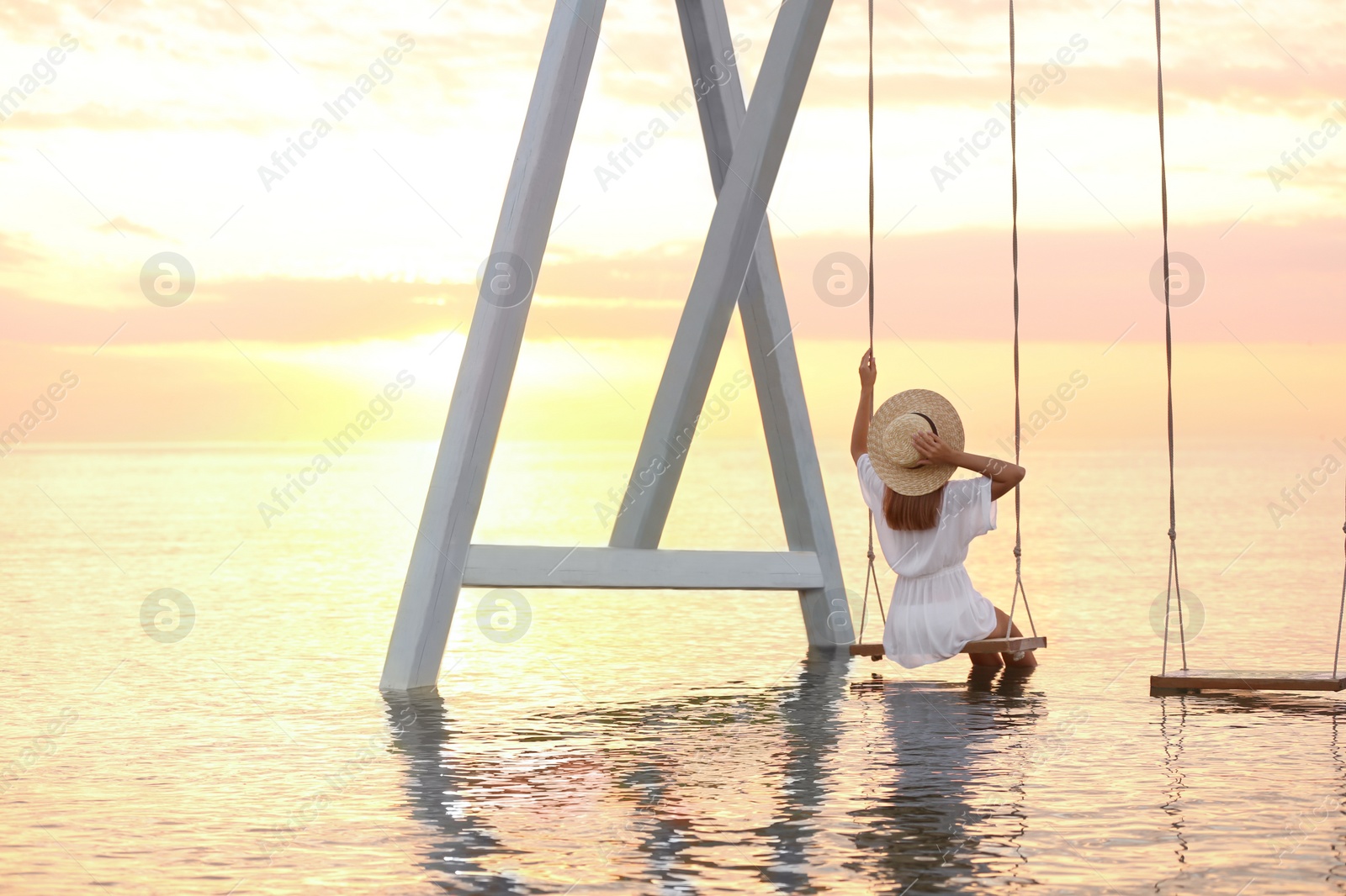 Photo of Young woman enjoying sunrise on swing over water