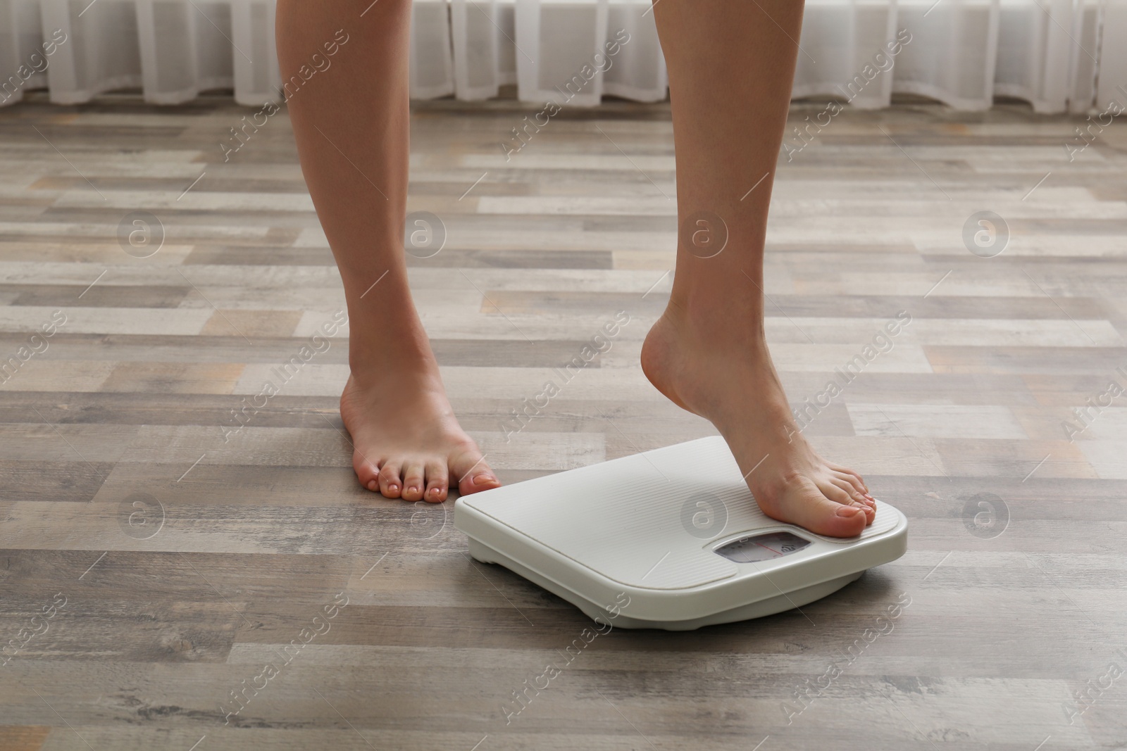 Photo of Woman stepping on floor scales indoors, closeup. Weight control