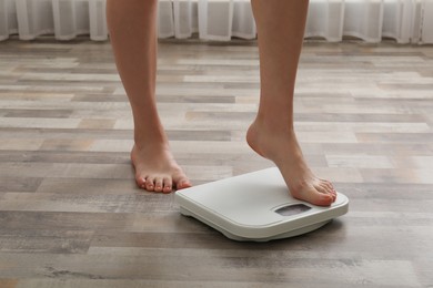 Woman stepping on floor scales indoors, closeup. Weight control