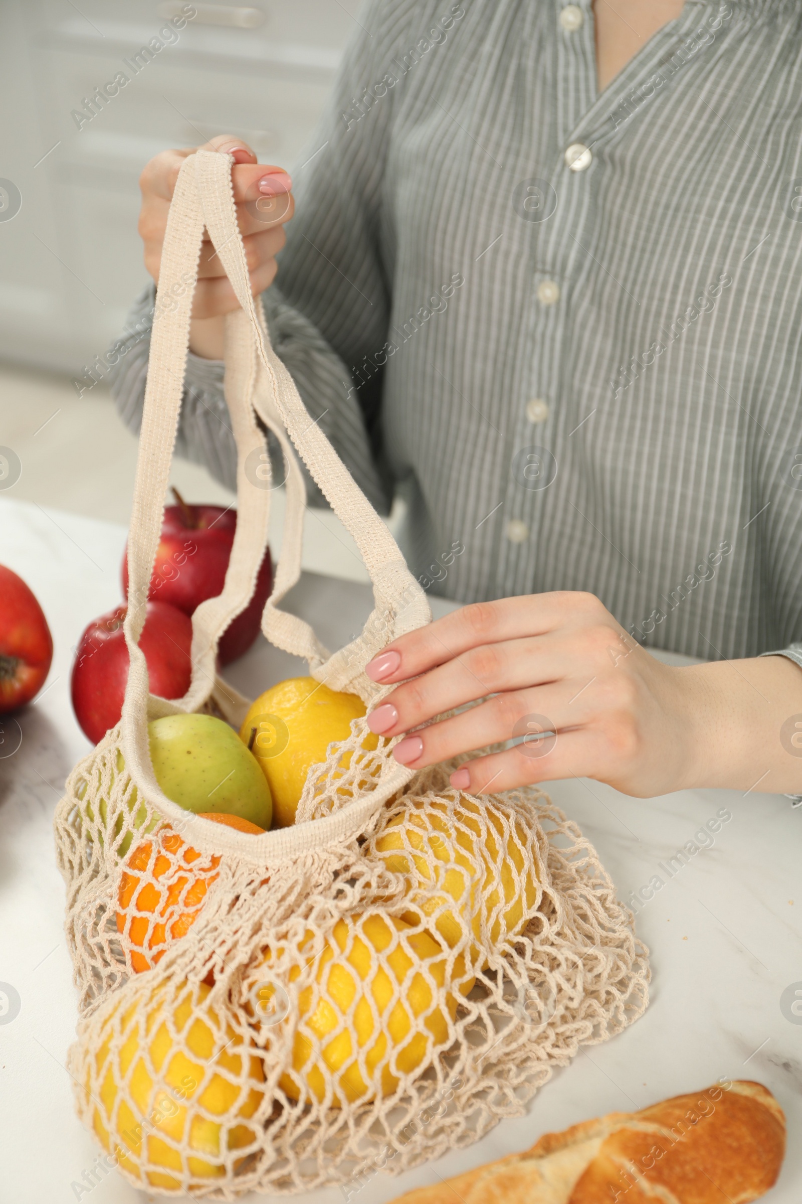 Photo of Woman with string bag of fresh fruits at light marble table, closeup