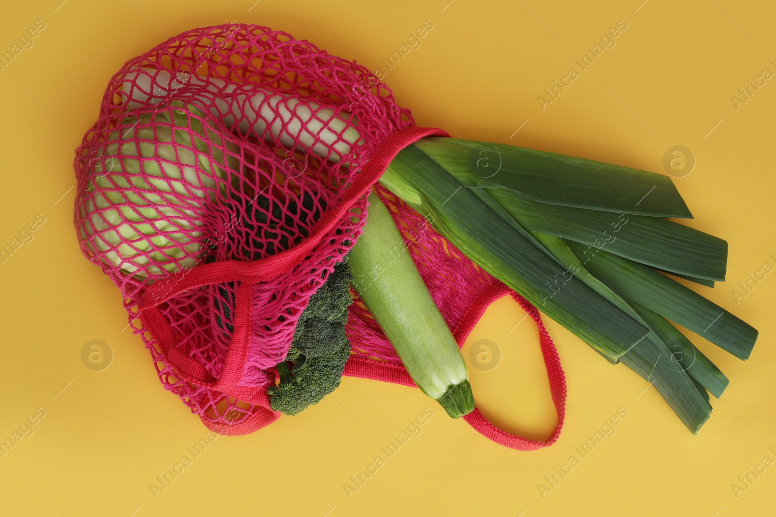 Photo of Net bag with vegetables on yellow background, top view