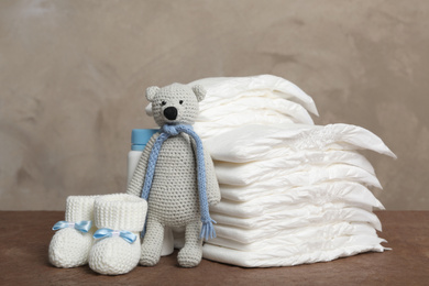 Photo of Baby diapers, toy bear and child's booties on wooden table