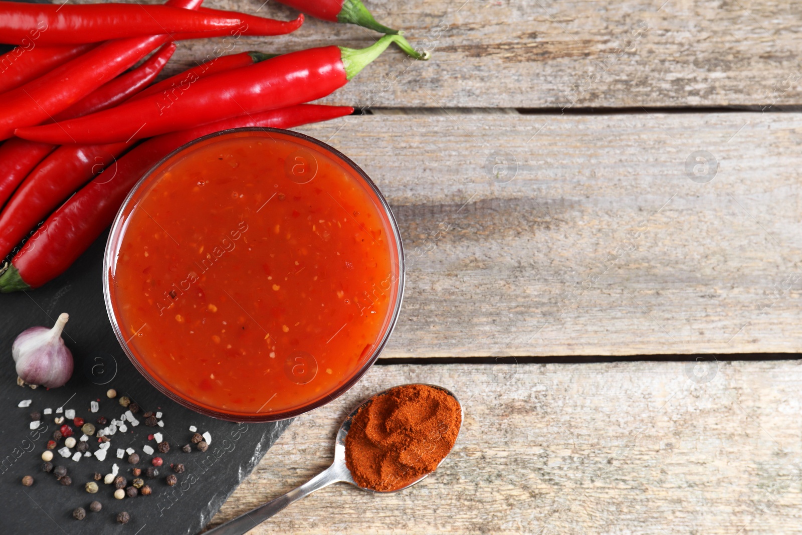 Photo of Spicy chili sauce in bowl and ingredients on wooden table, flat lay. Space for text