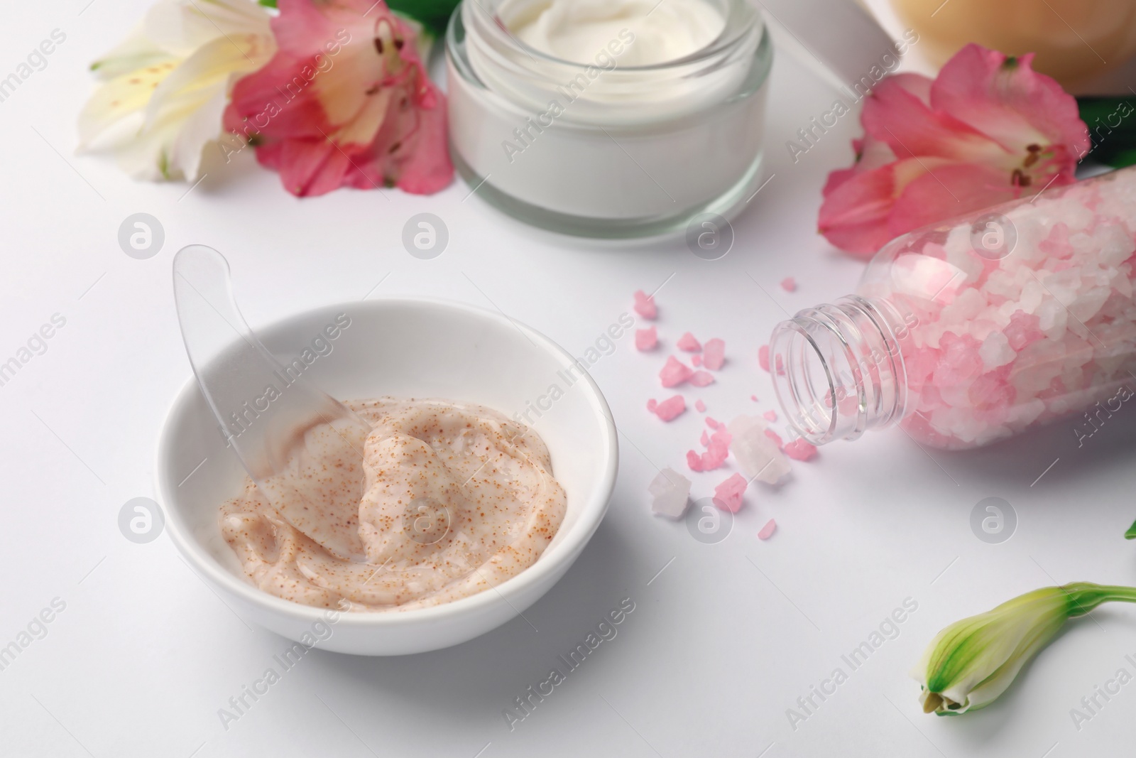 Photo of Bowl of scrub and sea salt on white table, closeup. Spa composition