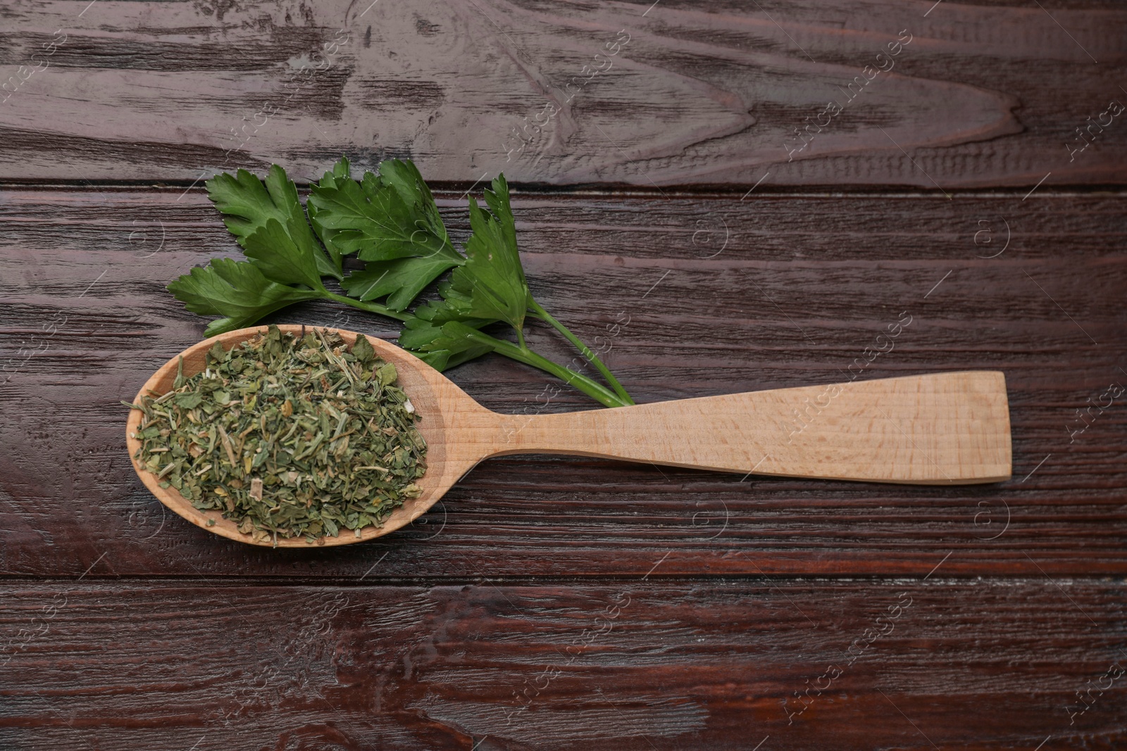 Photo of Spoon of dried aromatic parsley and fresh leaves on wooden table, flat lay