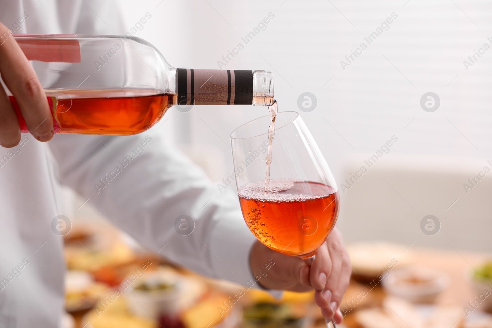 Photo of Man pouring rose wine from bottle into glass indoors, closeup