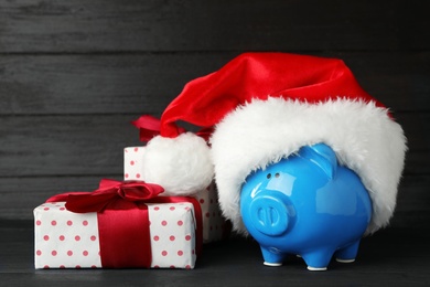 Photo of Piggy bank with Santa hat and gift boxes on black wooden table