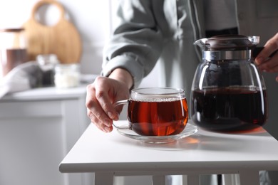 Woman with cup of hot tea at white table, closeup