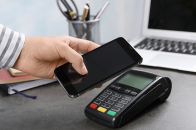 Photo of Woman using terminal for contactless payment with smartphone at table