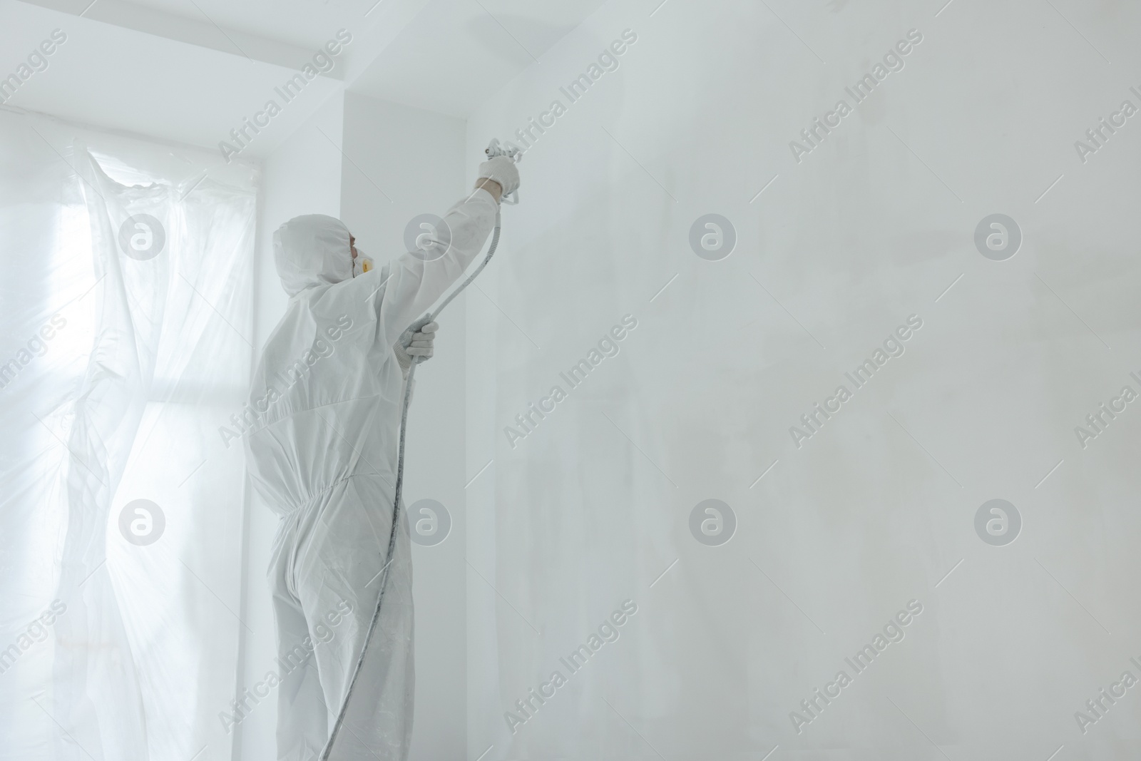 Photo of Decorator painting wall with spray indoors, space for text