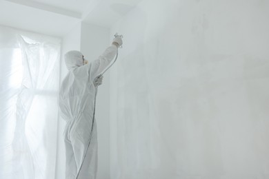 Photo of Decorator painting wall with spray indoors, space for text