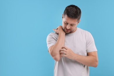 Photo of Allergy symptom. Man scratching his arm on light blue background. Space for text