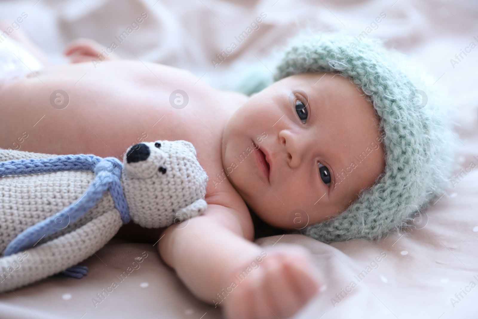 Photo of Cute newborn baby in warm hat with toy on bed