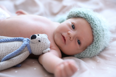 Photo of Cute newborn baby in warm hat with toy on bed