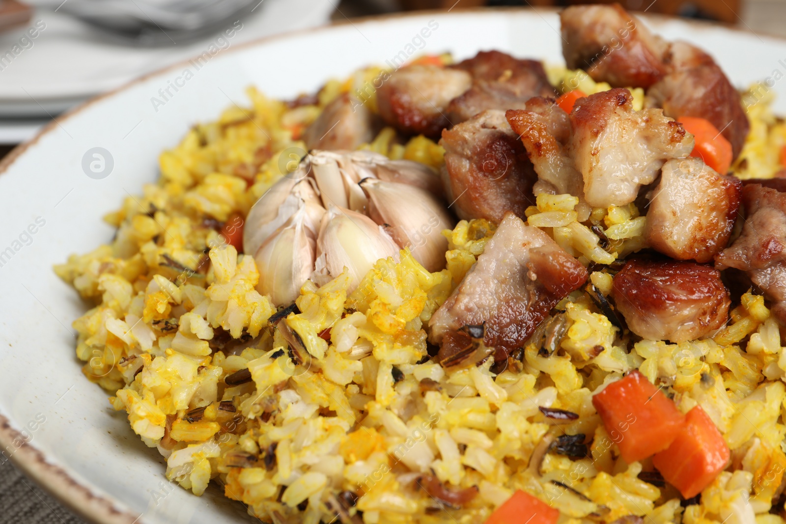 Photo of Delicious pilaf with meat, carrot and garlic on plate, closeup