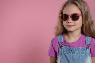 Girl in stylish sunglasses on pink background, space for text