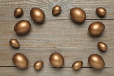 Frame of golden eggs on wooden table, flat lay. Space for text