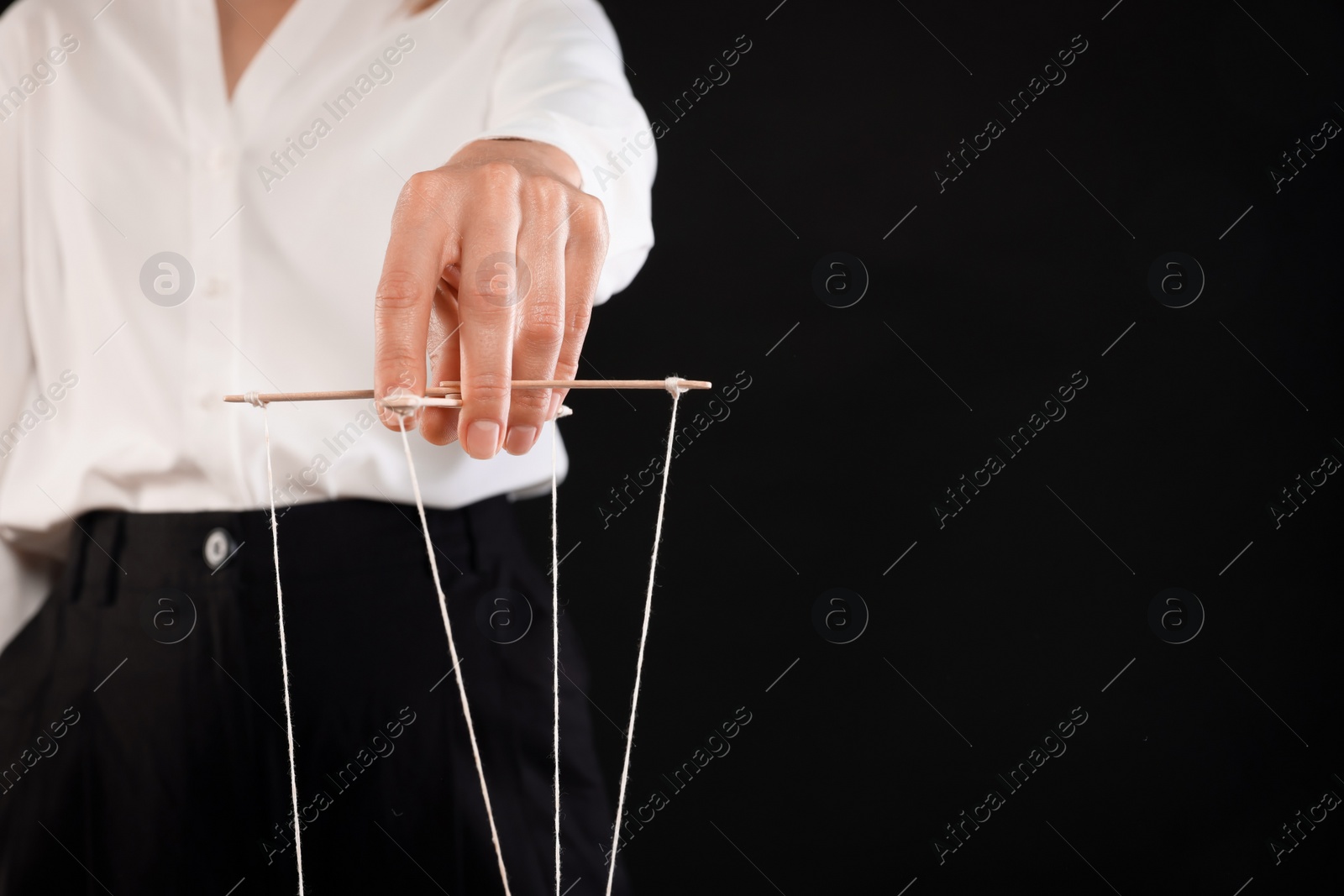 Photo of Woman in formal outfit pulling strings of puppet on black background, closeup. Space for text