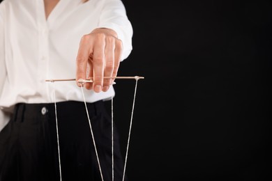 Photo of Woman in formal outfit pulling strings of puppet on black background, closeup. Space for text