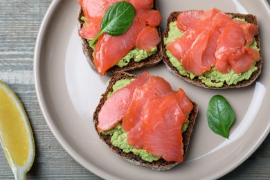 Photo of Delicious sandwiches with salmon and avocado on grey wooden table, flat lay