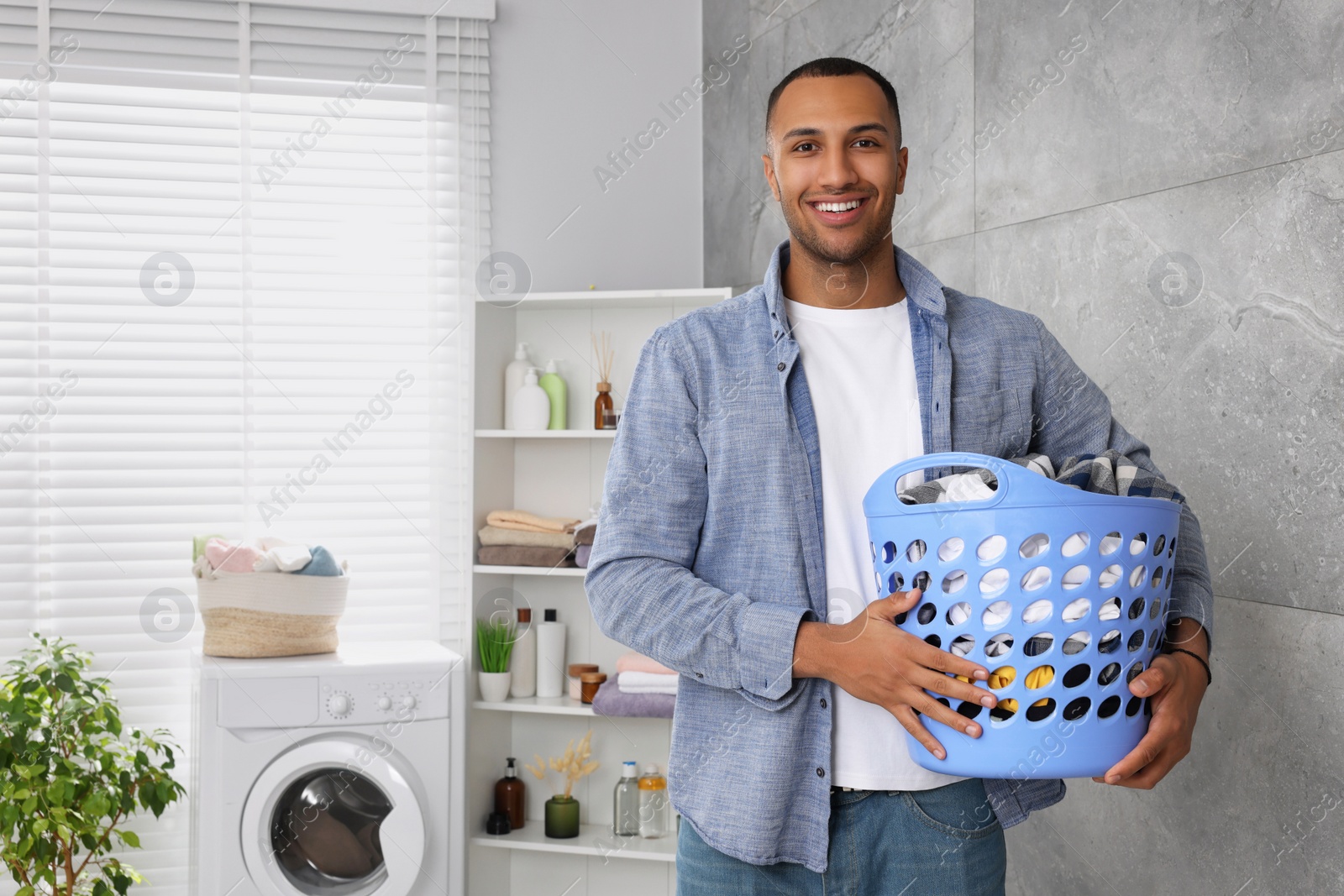 Photo of Happy man with basket full of laundry in bathroom. Space for text