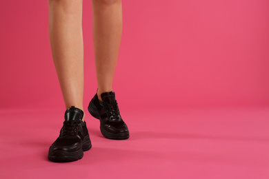 Photo of Woman wearing sneakers on pink background, closeup. Space for text