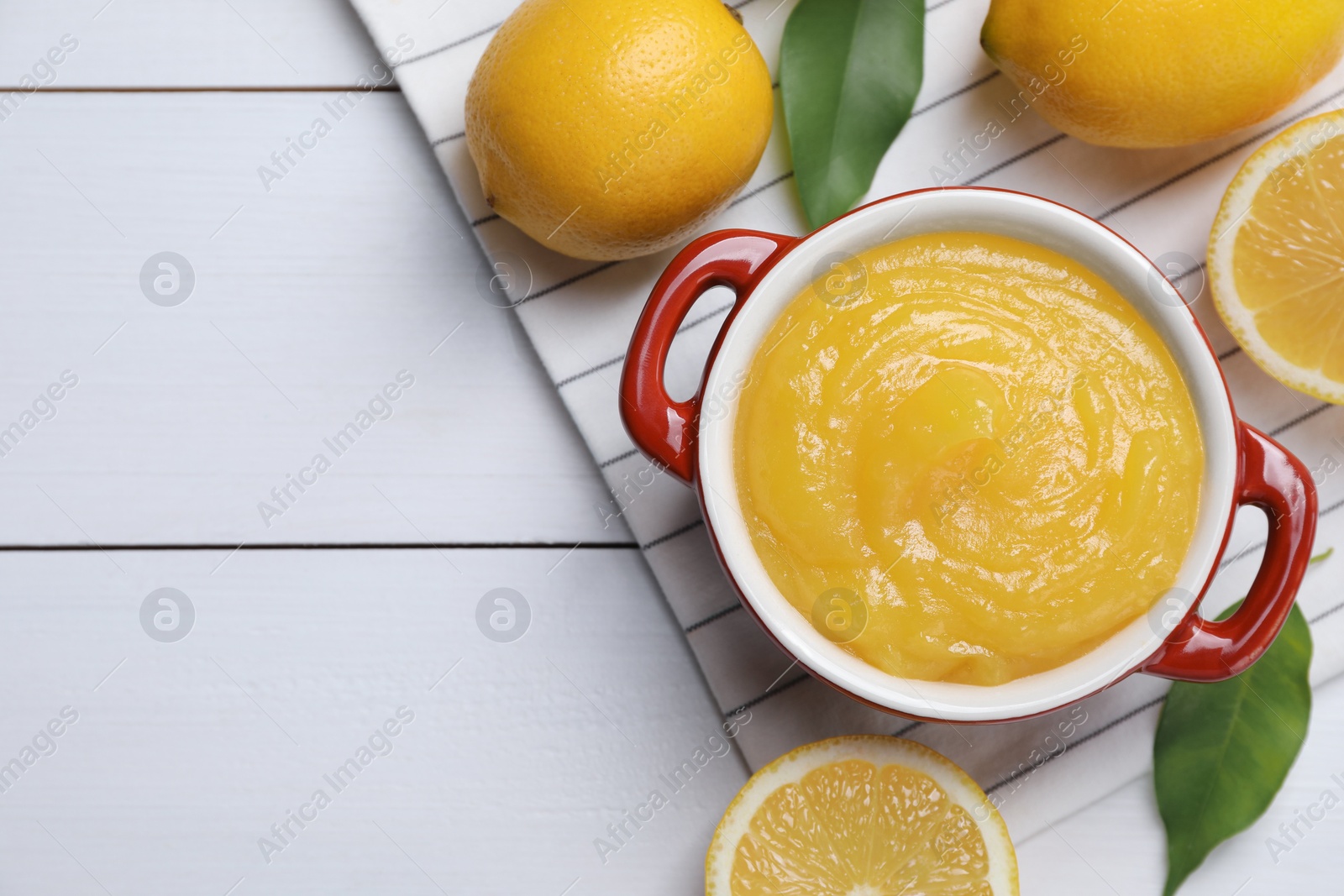 Photo of Delicious lemon curd in bowl and fresh citrus fruits on white wooden table, flat lay. Space for text