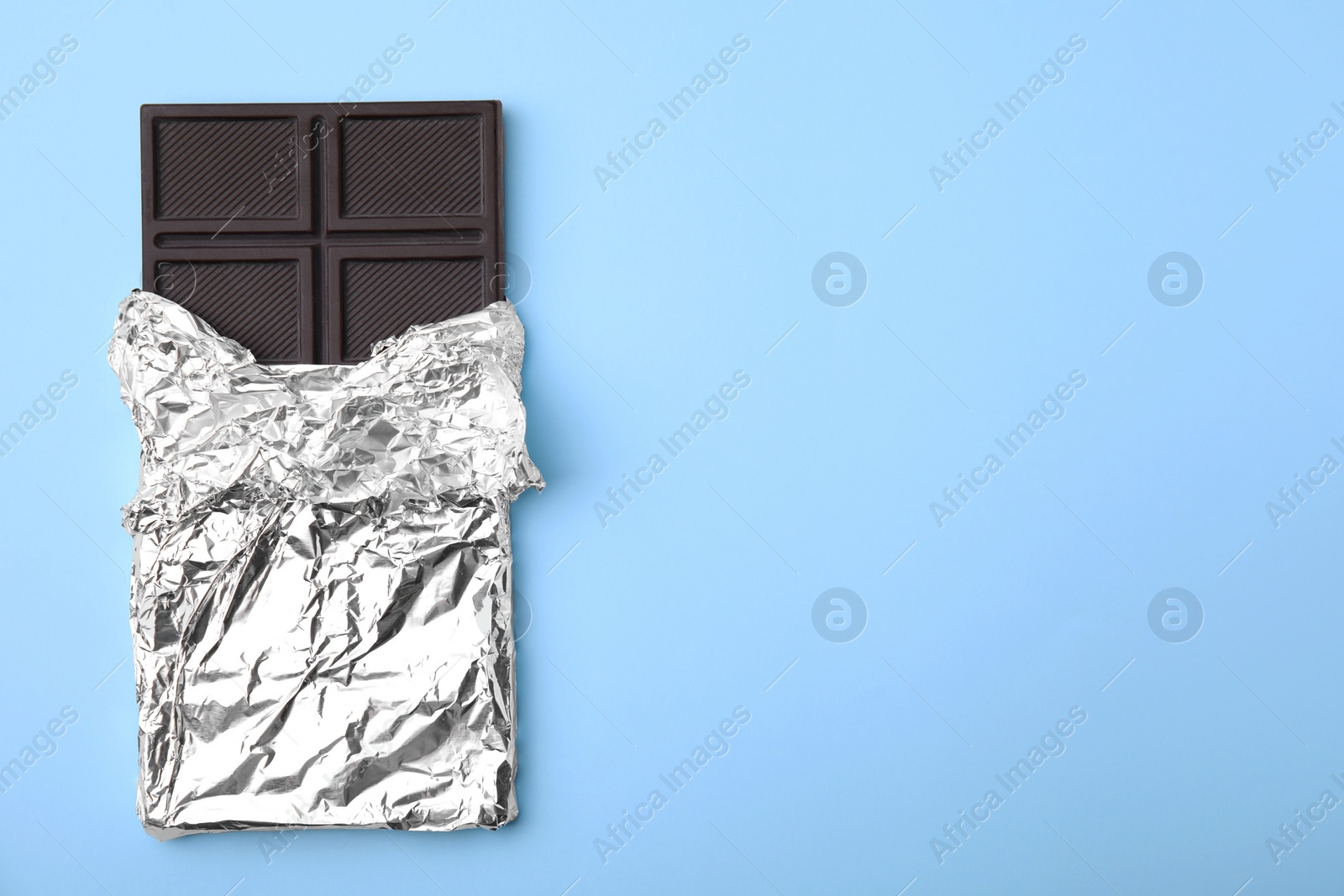 Photo of Tasty chocolate bar on light blue background, top view. Space for text